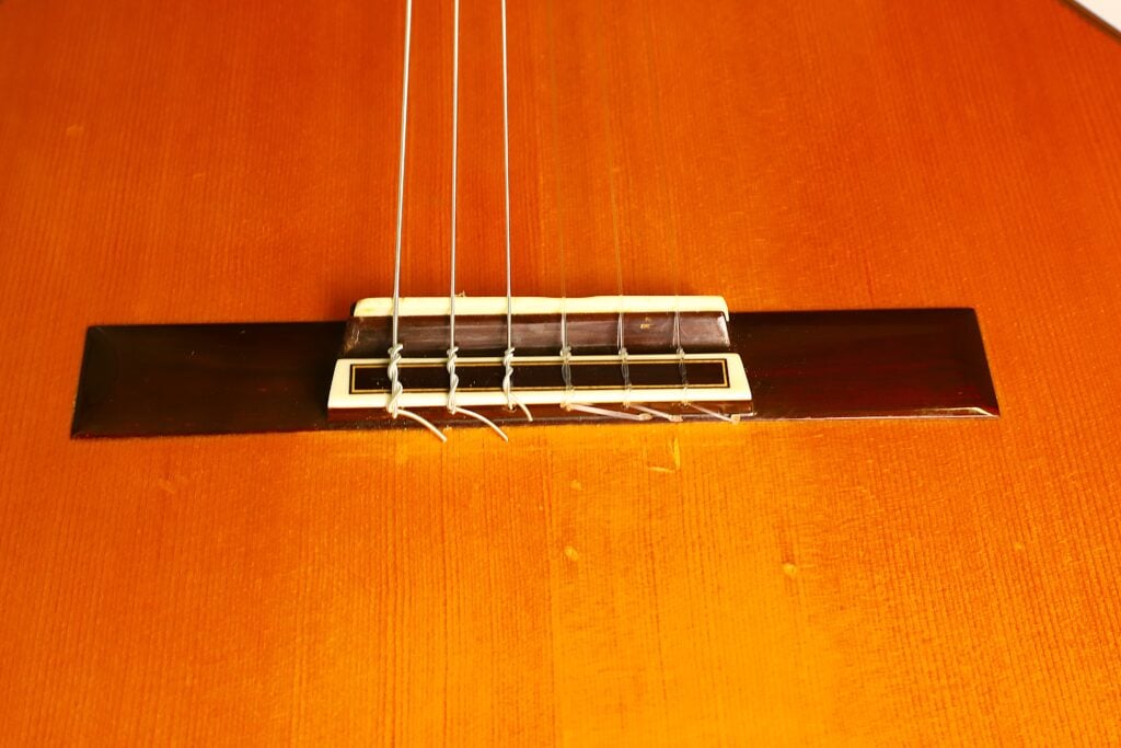 Nahaufnahme eines Stegs einer Masaru Kohno 1990 Professional J Klassische Gitarre mit festgebundenen Nylonsaiten. Nahaufnahme eines Stegs einer Masaru Kohno 1990 Professional J Klassische Gitarre mit festgebundenen Nylonsaiten.