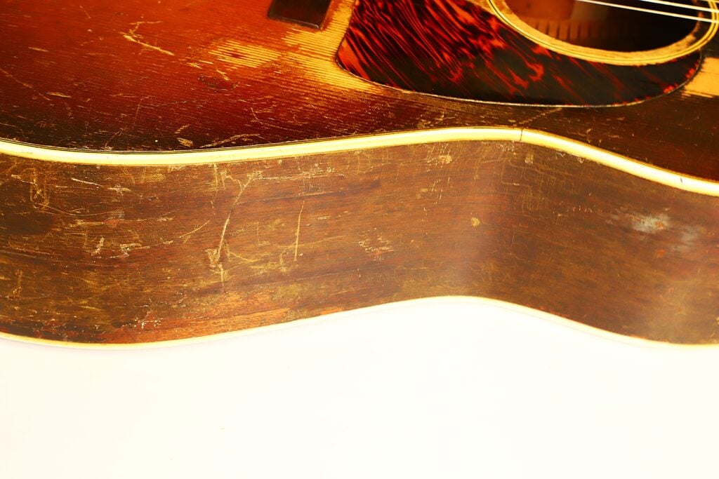 Nahaufnahme des abgenutzten Holzkorpus und des gemusterten Schlagbretts einer Gibson J-45 Banner Akustikgitarre aus dem Jahr 1943. Nahaufnahme des abgenutzten Holzkorpus und des gemusterten Schlagbretts einer Gibson J-45 Banner Akustikgitarre aus dem Jahr 1943.