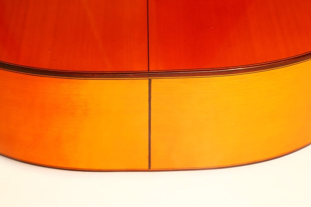 Nahaufnahme des Holzrückens einer Flamenco-Gitarre von Conde Hermanos aus dem Jahr 1989, auf der die Mittelnaht zu sehen ist, die zwei Holzplatten unterschiedlicher Farbnuance miteinander verbindet. Nahaufnahme des Holzrückens einer Flamenco-Gitarre von Conde Hermanos aus dem Jahr 1989, auf der die Mittelnaht zu sehen ist, die zwei Holzplatten unterschiedlicher Farbnuance miteinander verbindet.
