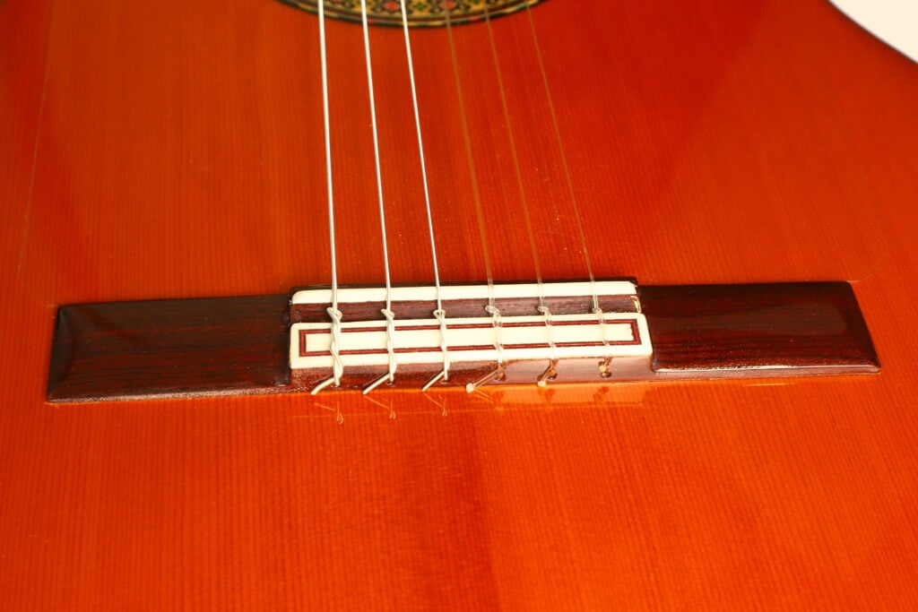Nahaufnahme des Stegs und der Nylonsaiten einer Flamenco-Gitarre von Conde Hermanos aus dem Jahr 1989. Nahaufnahme des Stegs und der Nylonsaiten einer Flamenco-Gitarre von Conde Hermanos aus dem Jahr 1989.