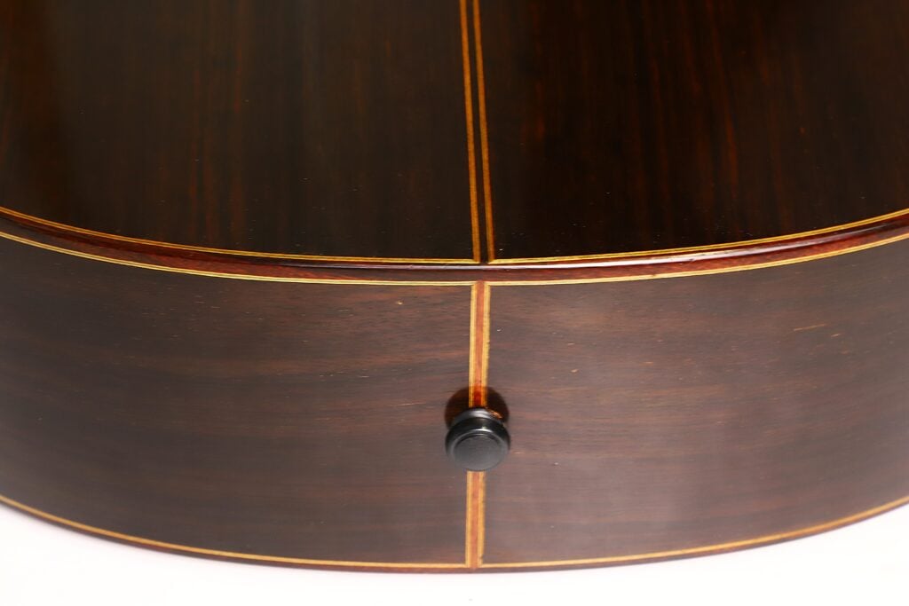 Nahaufnahme der unteren Wölbung einer Richard-Howell-Klassikgitarre aus dunklem Holz (Baujahr 1980), die die Mittelnaht, die Zierleiste und den Saitenhalter zeigt. Nahaufnahme der unteren Wölbung einer Richard-Howell-Klassikgitarre aus dunklem Holz (Baujahr 1980), die die Mittelnaht, die Zierleiste und den Saitenhalter zeigt.