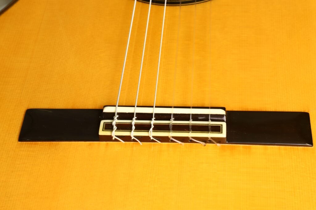 Nahaufnahme eines Sattels einer Antonio Aparicio Master Flamenco-Gitarre, an dem Nylonsaiten befestigt sind. Nahaufnahme eines Sattels einer Antonio Aparicio Master Flamenco-Gitarre, an dem Nylonsaiten befestigt sind.