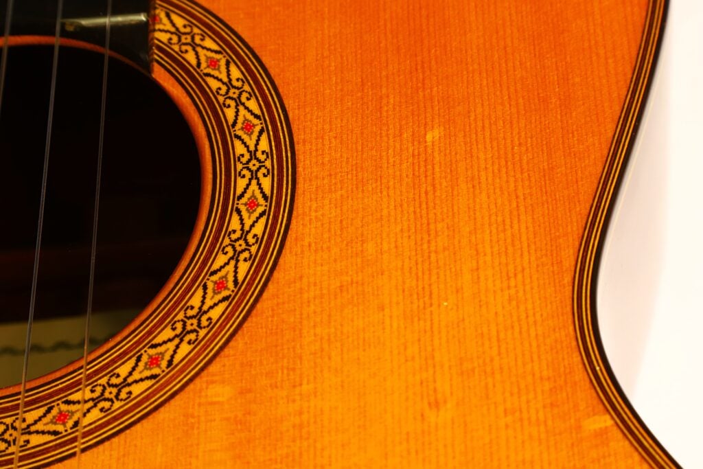 Nahaufnahme des Korpus einer Masaru Kohno 1990 Professional J Klassische Gitarre, die das Schallloch mit einer kunstvoll verzierten Rosette mit geometrischen Mustern und einer Holzrandeinlage zeigt. Nahaufnahme des Korpus einer Masaru Kohno 1990 Professional J Klassische Gitarre, die das Schallloch mit einer kunstvoll verzierten Rosette mit geometrischen Mustern und einer Holzrandeinlage zeigt.