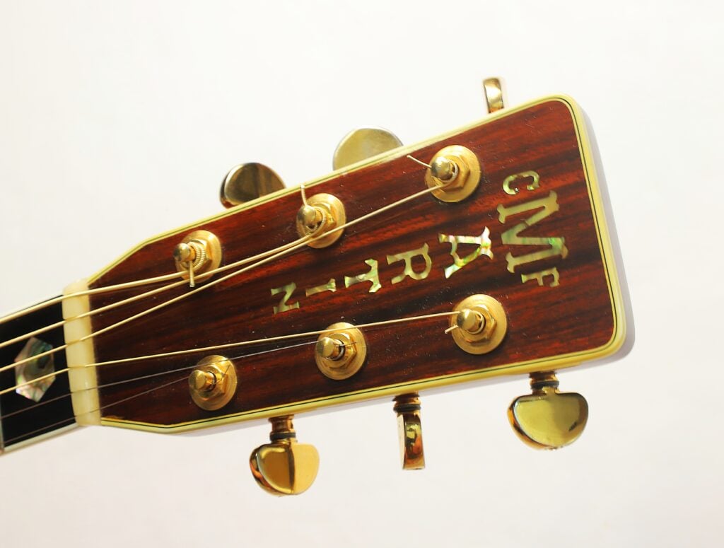 Kopfplatte einer Martin SOM-45 Akustikgitarre aus dem Jahr 1977 mit goldenen Stimmwirbeln und einer Einlage aus Perlmutt mit der Aufschrift CF MARTIN. Kopfplatte einer Martin SOM-45 Akustikgitarre aus dem Jahr 1977 mit goldenen Stimmwirbeln und einer Einlage aus Perlmutt mit der Aufschrift CF MARTIN.