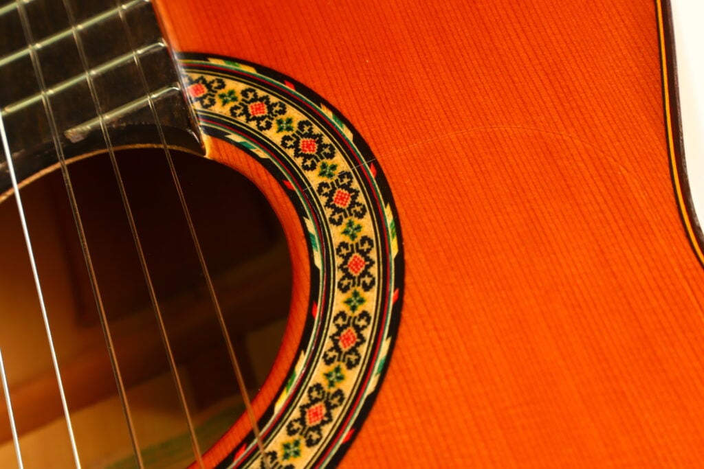 Nahaufnahme des Schalllochs einer Flamenco-Gitarre von Conde Hermanos aus dem Jahr 1989 mit einer farbenfrohen, aufwendig gestalteten Mosaikrosette. Nahaufnahme des Schalllochs einer Flamenco-Gitarre von Conde Hermanos aus dem Jahr 1989 mit einer farbenfrohen, aufwendig gestalteten Mosaikrosette.