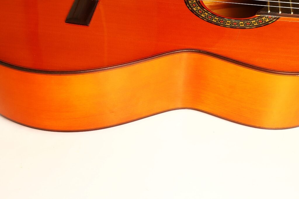 Nahaufnahme des Korpus aus Orangenholz einer Flamenco-Gitarre von Conde Hermanos aus dem Jahr 1989, auf der das Schallloch mit einer Rosette mit dekorativem Muster zu sehen ist. Nahaufnahme des Korpus aus Orangenholz einer Flamenco-Gitarre von Conde Hermanos aus dem Jahr 1989, auf der das Schallloch mit einer Rosette mit dekorativem Muster zu sehen ist.