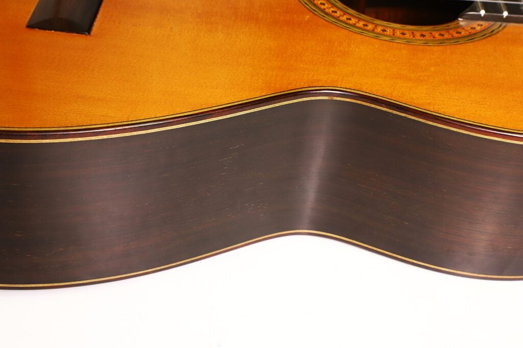Nahaufnahme des Mittelstücks und der Decke einer Klassischen Gitarre von Richard Howell aus dem Jahr 1980 mit dunklen Holzseiten und einer helleren Fichtendecke. Nahaufnahme des Mittelstücks und der Decke einer Klassischen Gitarre von Richard Howell aus dem Jahr 1980 mit dunklen Holzseiten und einer helleren Fichtendecke.