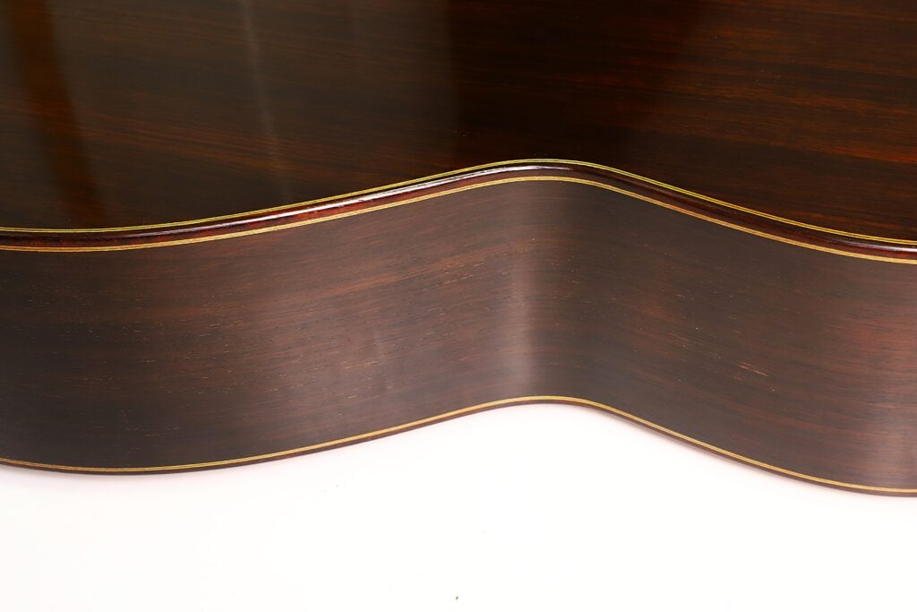 Nahaufnahme des Korpus aus dunklem Holz und der geschwungenen Taille einer Klassische Gitarre von Richard Howell aus dem Jahr 1980 mit schmalen, hellen Zierleisten. Nahaufnahme des Korpus aus dunklem Holz und der geschwungenen Taille einer Klassische Gitarre von Richard Howell aus dem Jahr 1980 mit schmalen, hellen Zierleisten.