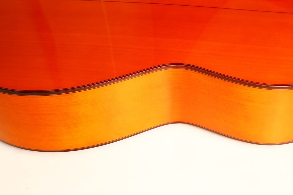 Nahaufnahme der gewölbten Seite und Oberseite einer orangefarbenen Flamenco-Gitarre von Conde Hermanos aus dem Jahr 1989. Nahaufnahme der gewölbten Seite und Oberseite einer orangefarbenen Flamenco-Gitarre von Conde Hermanos aus dem Jahr 1989.