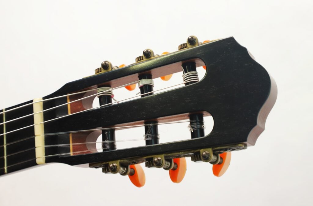 Geschlitzter Kopf einer Torres Klassische Gitarre von Matthias Hartig aus dem Jahr 2021 mit dunklem Holz, goldfarbenen Stimmmechaniken und orangefarbenen Stimmknöpfen. Geschlitzter Kopf einer Torres Klassische Gitarre von Matthias Hartig aus dem Jahr 2021 mit dunklem Holz, goldfarbenen Stimmmechaniken und orangefarbenen Stimmknöpfen.