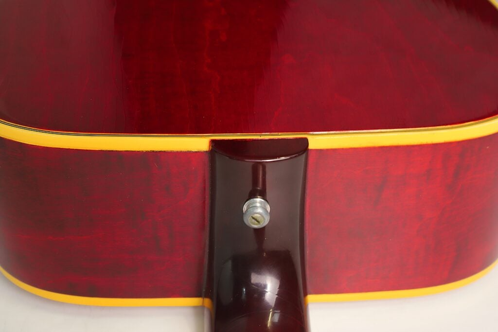 Nahaufnahme des Halsfußbereichs und des Riemenknopfs am Korpus einer kirschroten Gibson Dove Akustikgitarre aus dem Jahr 1968. Nahaufnahme des Halsfußbereichs und des Riemenknopfs am Korpus einer kirschroten Gibson Dove Akustikgitarre aus dem Jahr 1968.