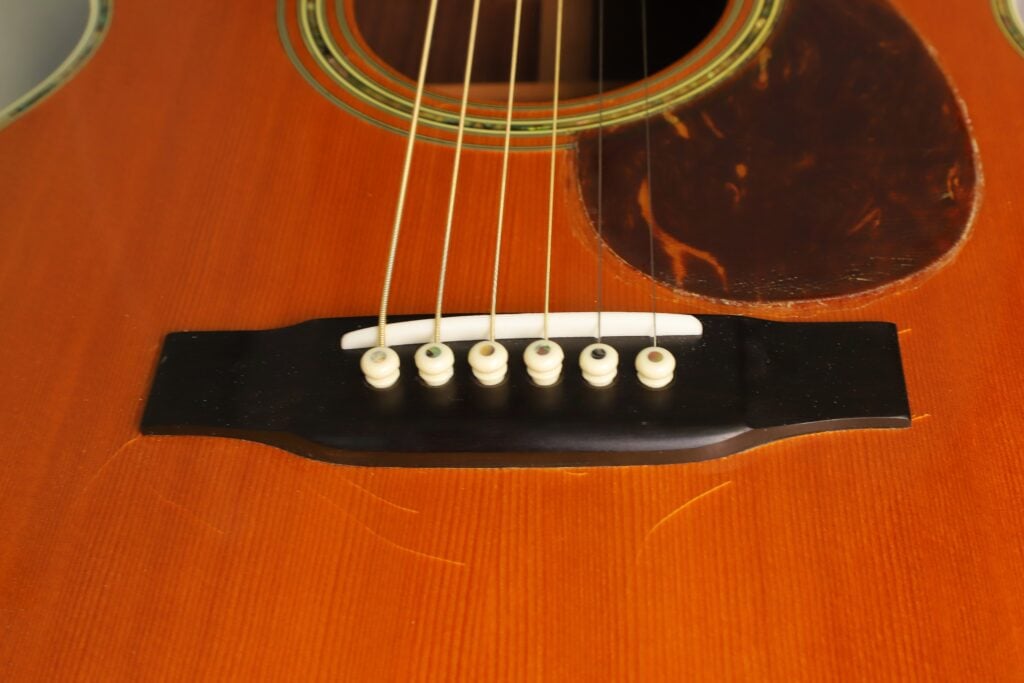 Nahaufnahme des Stegs, des Sattels und der Saiten über dem Holzkorpus einer Martin SOM-45 Akustikgitarre aus dem Jahr 1977. Nahaufnahme des Stegs, des Sattels und der Saiten über dem Holzkorpus einer Martin SOM-45 Akustikgitarre aus dem Jahr 1977.