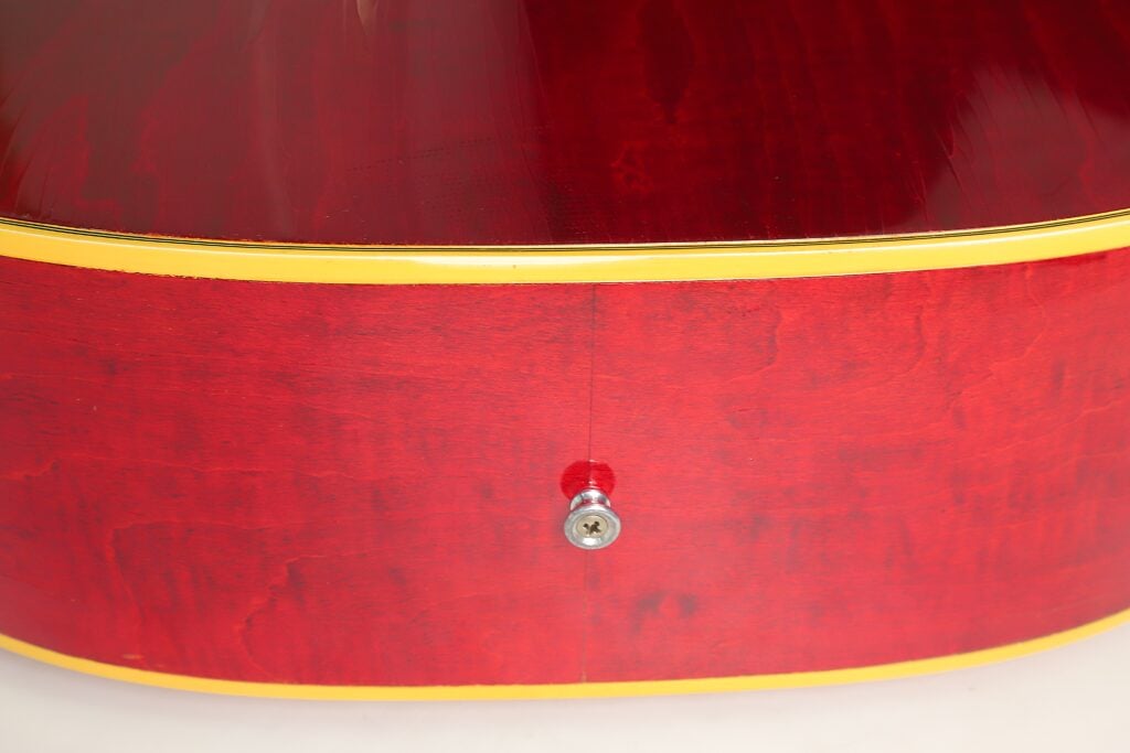 Nahaufnahme der rot lackierten Unterseite einer Gibson Dove Akustikgitarre aus dem Jahr 1968, auf der ein Metall-Gurtknopf zu sehen ist. Nahaufnahme der rot lackierten Unterseite einer Gibson Dove Akustikgitarre aus dem Jahr 1968, auf der ein Metall-Gurtknopf zu sehen ist.