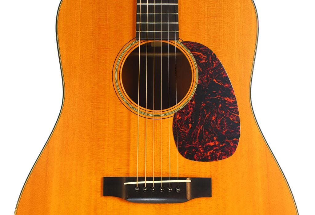Nahaufnahme des Korpus einer Martin D-18 VS 2006 Klassische Gitarre mit einem dunklen Pickguard in Schildpattoptik, einem runden Schallloch und einem dunklen Steg mit sechs Saiten. Nahaufnahme des Korpus einer Martin D-18 VS 2006 Klassische Gitarre mit einem dunklen Pickguard in Schildpattoptik, einem runden Schallloch und einem dunklen Steg mit sechs Saiten.