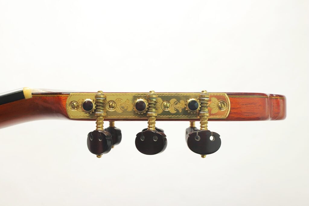 Seitenansicht des Kopfes einer Hopf Gran Concertio 2000 Klassische Gitarre mit verzierten goldenen Stimmplatten und dunklen Stimmwirbeln. Seitenansicht des Kopfes einer Hopf Gran Concertio 2000 Klassische Gitarre mit verzierten goldenen Stimmplatten und dunklen Stimmwirbeln.