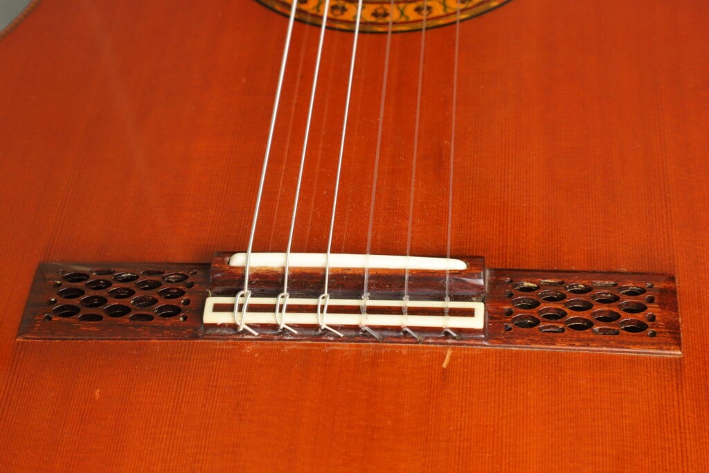 Nahaufnahme eines Sattels der Hopf Gran Concertio 2000 Klassische Gitarre mit dekorativen Ausschnitten und einem weißen Sattel auf einem Holzkorpus. Nahaufnahme eines Sattels der Hopf Gran Concertio 2000 Klassische Gitarre mit dekorativen Ausschnitten und einem weißen Sattel auf einem Holzkorpus.