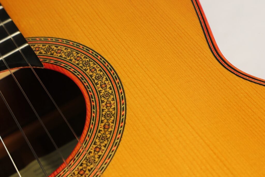 Nahaufnahme einer Torres Klassische Gitarre von Matthias Hartig aus dem Jahr 2021, die das Schallloch, die aufwendig verzierte Rosette und die Holzdecke zeigt. Nahaufnahme einer Torres Klassische Gitarre von Matthias Hartig aus dem Jahr 2021, die das Schallloch, die aufwendig verzierte Rosette und die Holzdecke zeigt.
