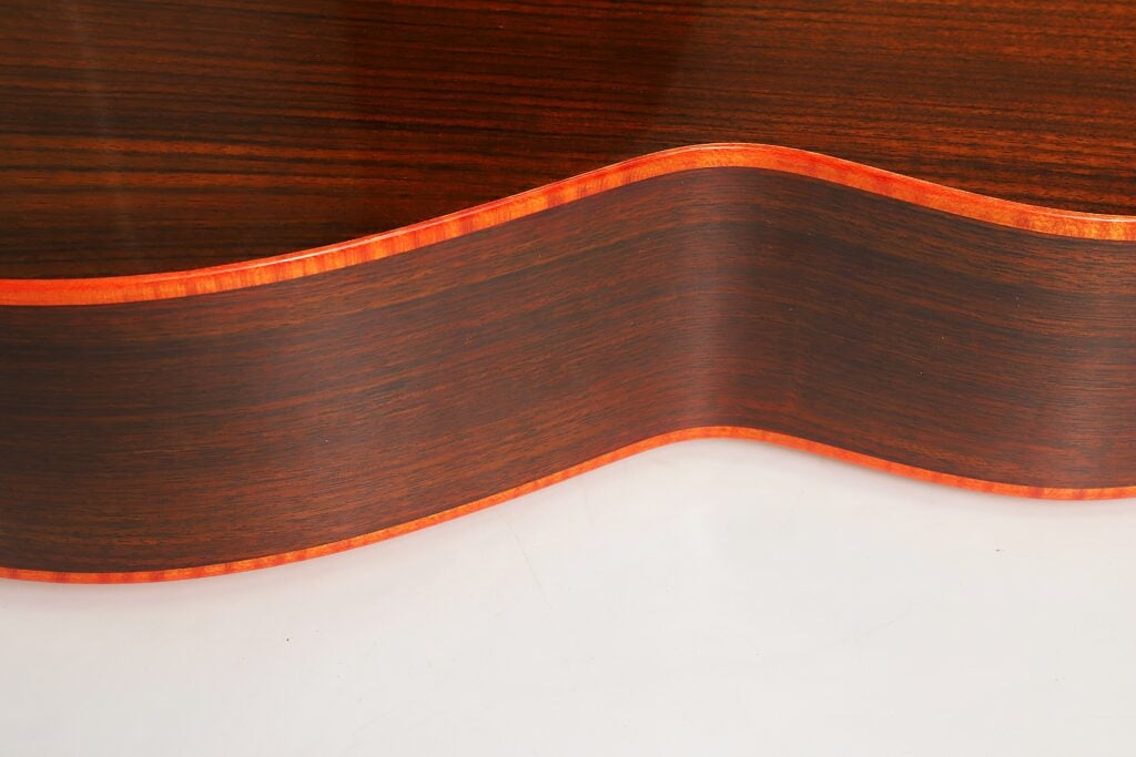 Nahaufnahme des Korpus einer Torres Klassische Gitarre von Matthias Hartig aus dem Jahr 2021 aus dunklem Holz mit leuchtend orangefarbener Kantenverzierung. Nahaufnahme des Korpus einer Torres Klassische Gitarre von Matthias Hartig aus dem Jahr 2021 aus dunklem Holz mit leuchtend orangefarbener Kantenverzierung.