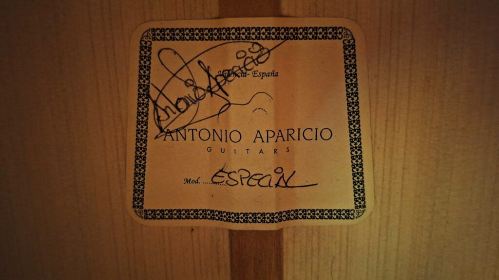 Ein rechteckiges Etikett im Schallloch einer Antonio Aparicio Master Flamenco-Gitarre mit einer Zierbordüre, dem Schriftzug Antonio Aparicio Guitars, einer handschriftlichen Unterschrift und der Modellbezeichnung Especial. Ein rechteckiges Etikett im Schallloch einer Antonio Aparicio Master Flamenco-Gitarre mit einer Zierbordüre, dem Schriftzug Antonio Aparicio Guitars, einer handschriftlichen Unterschrift und der Modellbezeichnung Especial.