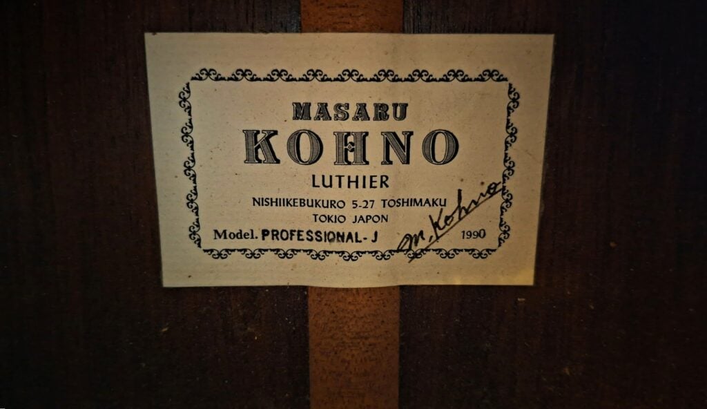 Ein rechteckiges Papieretikett für eine Masaru Kohno 1990 Professional J Klassische Gitarre mit verzierten Rändern, auf dem der Name des Herstellers, das Modell, das Baujahr und eine handschriftliche Unterschrift zu lesen sind. Ein rechteckiges Papieretikett für eine Masaru Kohno 1990 Professional J Klassische Gitarre mit verzierten Rändern, auf dem der Name des Herstellers, das Modell, das Baujahr und eine handschriftliche Unterschrift zu lesen sind.
